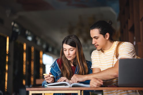 Two students study together in a library, collaborating on a project and preparing for exams.