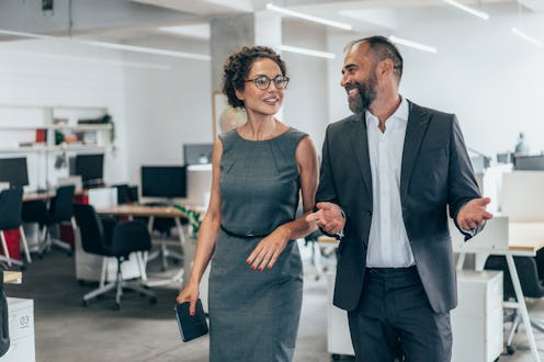 Two smiling business people walking through office hall and talking. Business coworkers walking tog...