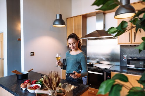 Mid adult woman in a modern kitchen looking at her smartphone while preparing a meal with fresh vege...