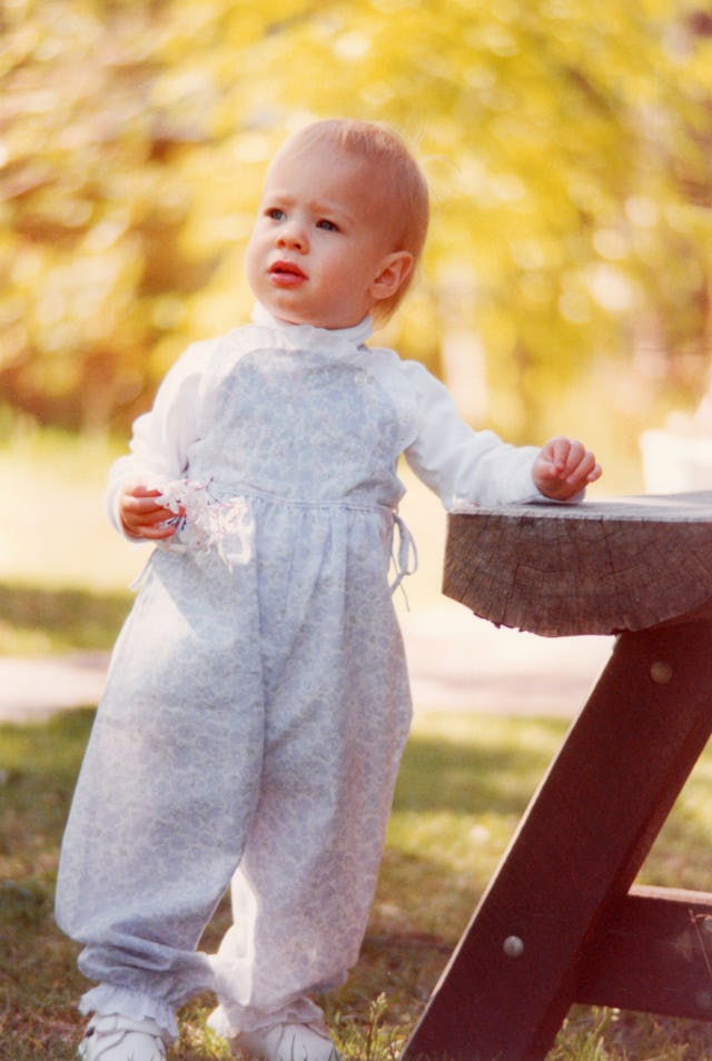 A toddler stands next to bench seat on her first birthday holding jasmine flowers.