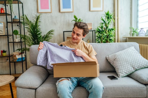 Young cheerful man unpacking box after online shopping