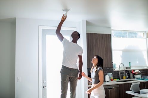 An African American man and Chinese American woman install a lightbulb with smart device technology ...