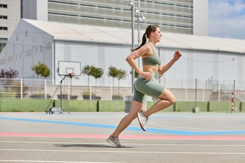 Young woman is running fast on a running track in an urban environment, giving her best during a spo...