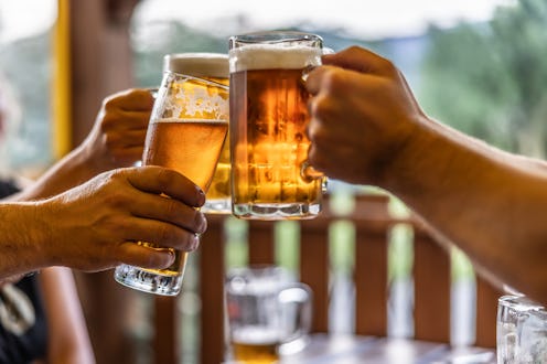 Group of friends toasting with beer on the terrace during hot summer days. Close-up of a group of pe...
