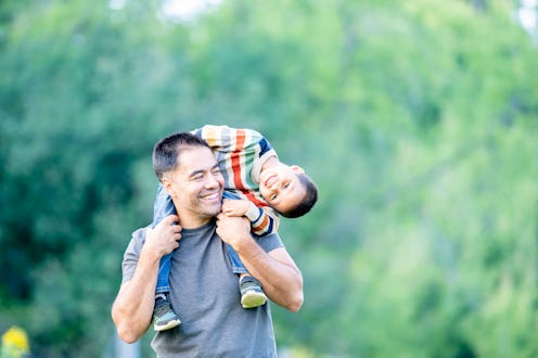A sweet little mixed race boy sits atop his Fathers shoulders as he carries him during a fall walk t...