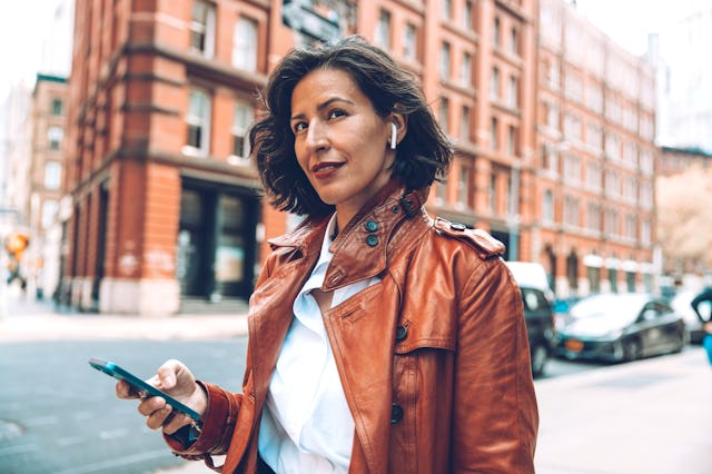 Elegant businesswoman walking to the office listening voice messages on earphones in downtown New Yo...