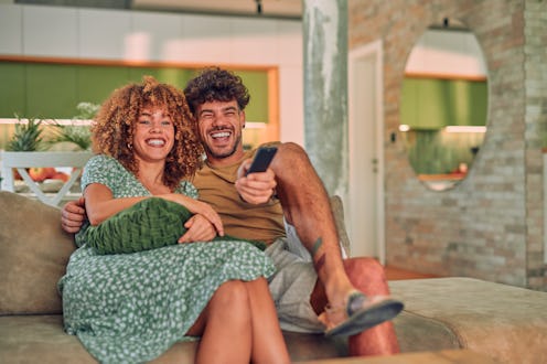 Couple Watches TV together while Sitting on a Couch in the Living Room. Girlfriend and Boyfriend emb...