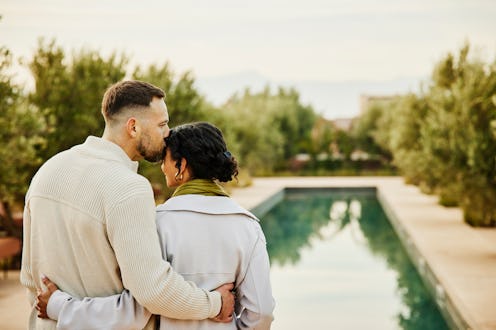 Medium shot of husband kissing wife on forehead while watching sunrise beside pool at boutique luxur...
