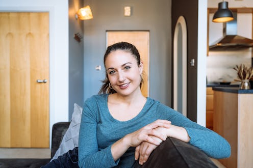 A young woman with a friendly smile sitting on a couch in a modern and cozy living room.