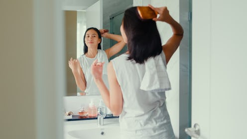 Young Asian woman having fun combing her beautiful hair in front of mirror in lavatory at home late ...