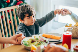 Portrait of an adorable little boy holding hands in prayer with his mother and grandmother on Christ...
