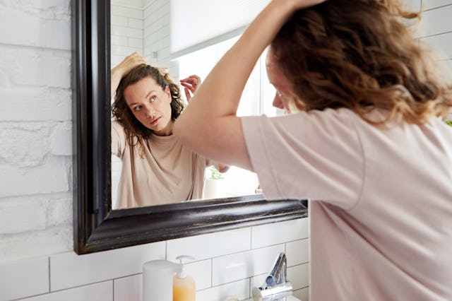 In a modern bathroom, a young person is grooming their hair in front of the mirror, emphasizing dail...