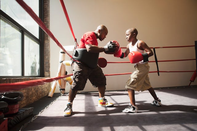 A child hits focus mitts in a boxing ring with his coach, in a story about sports kids can start lat...