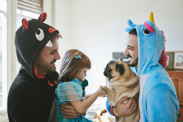 Happy couple in costumes carrying daughter and pug, in a story about the best dog breeds for familie...