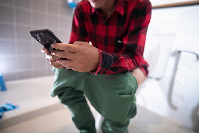 A man using a smart phone while sitting on the toilet. Doctors are recommending that people don't us...