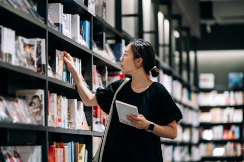 Young Asian woman looking at books at a bookstore. Female customer shopping for books at bookshop. M...
