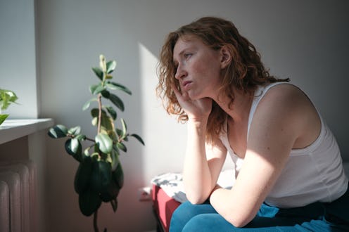 Sad depressed woman sitting on bed touching head suffering from headache. Migraine symptoms