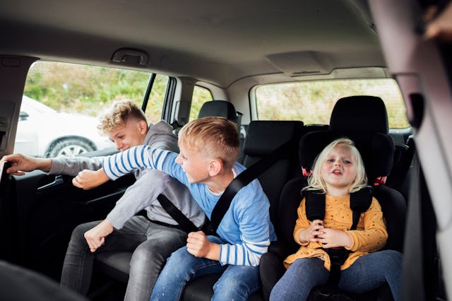 Three caucasian siblings of different ages sitting in the back of a car. The little girl is distress...