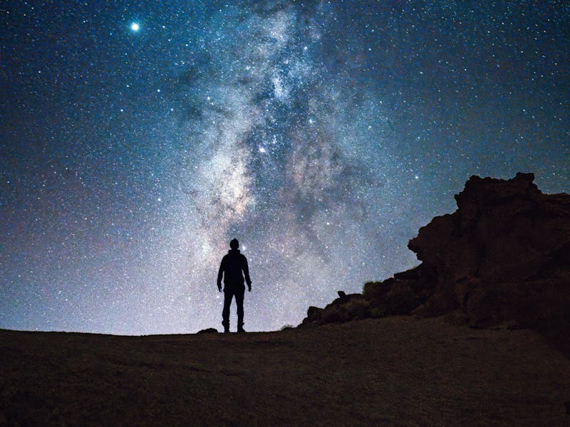 A silhouette of a person stands against the stunning backdrop of the Milky Way, visible in the clear...
