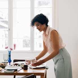A smiling Latin American woman setting the dining table for lunch.