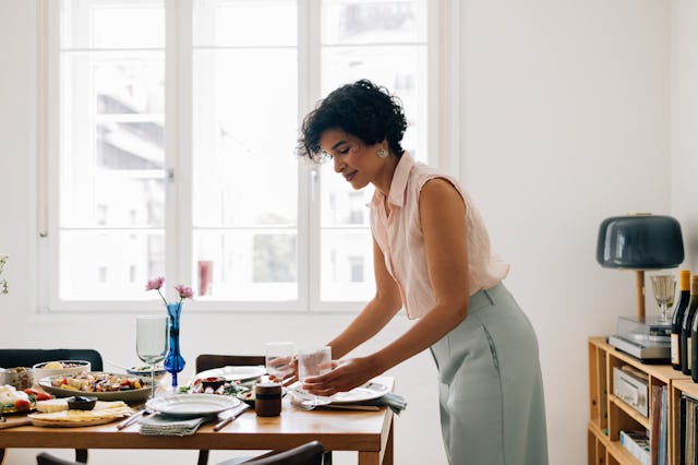 A smiling Latin American woman setting the dining table for lunch.