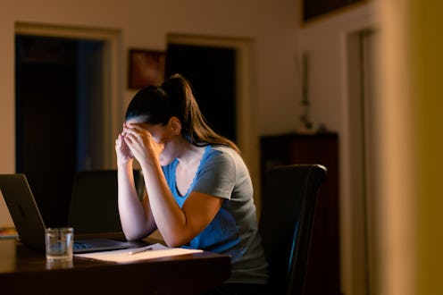 A young woman sits at a desk, overwhelmed and stressed, while working late at home.