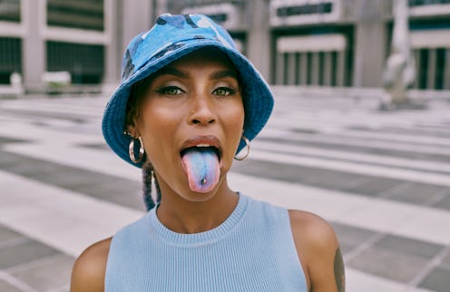 Shot of a trendy young woman sticking out her blue coloured tongue and showing her piercing against ...