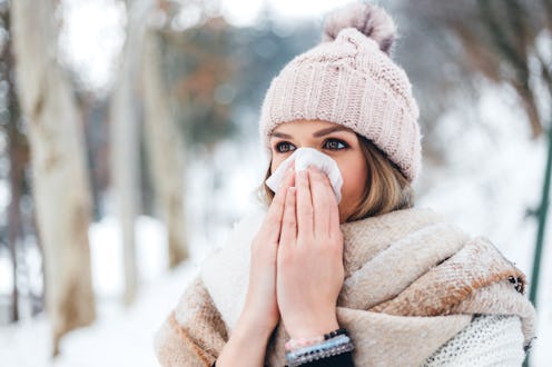 Beautiful young woman blowing her nose in a snowy park in winter.