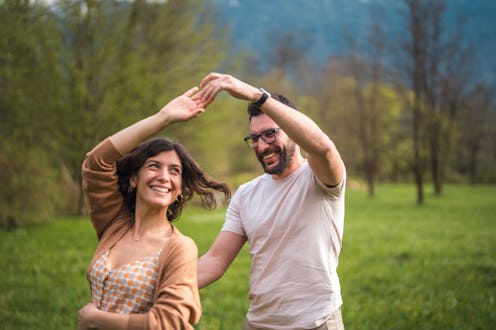 A smiling Hispanic mid-adult male and Caucasian female enjoy a dance on lush greenery at a boutique ...