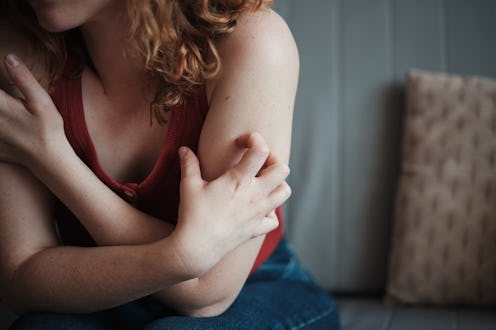 Close up of nervous stressed woman itching her skin, sitting on sofa at home, feeling anxious. Stres...