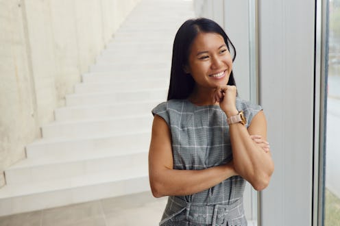 Happy Asian female entrepreneur day dreaming while standing in a hallway of an office building and l...