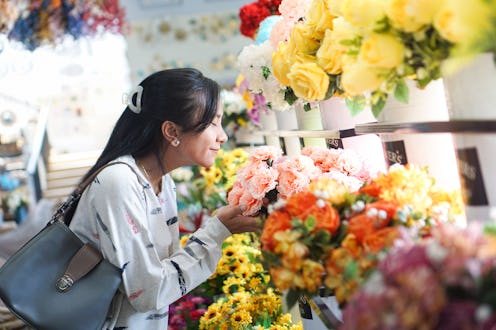 A woman in a casual sweater is smelling vibrant flowers from wooden crates in a well-lit flower shop...