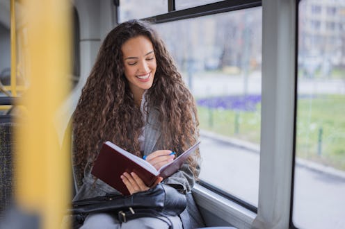 Happy young female student taking notes in a notebook during a bus ride