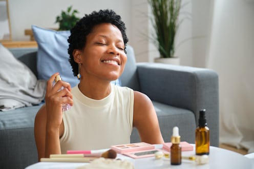 Beautiful mixed race woman applying perfume while getting ready on the floor at home