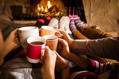 Four people warming their feet by the fireplace and drinking hot chocolate.