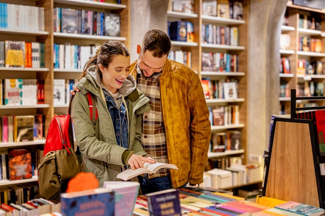 A young man and woman are checking out the latest literary offerings at a trendy book store, excited...