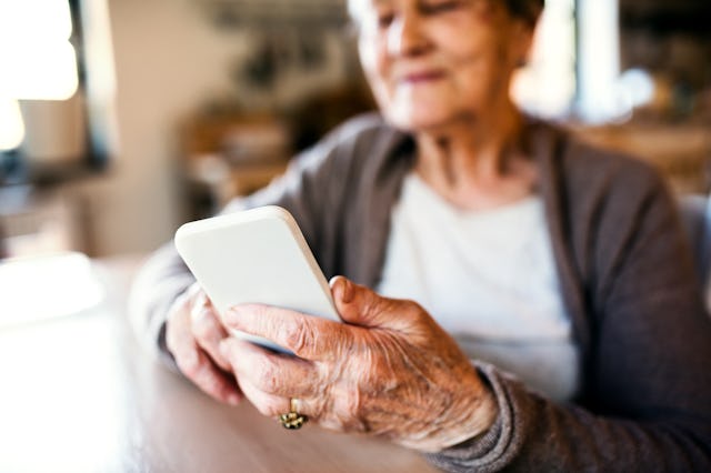 Beautiful grandmother at home sitting at the table and using smart phone.