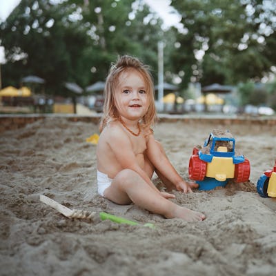 Happy little girl enjoying while playing in sand with her toys. Leica M6, ektar 100. The negative is a high-resolution 35mm film, manually arranged and cleaned, small dust particles and scratches can be seen.