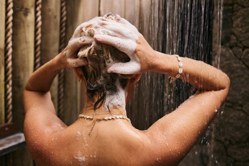 Rear view of carefree woman washing her hair with shampoo under the shower.