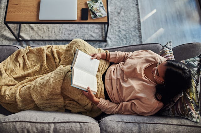 High angle shot of a young woman reading a book on the sofa at home, in a story about feel good book...
