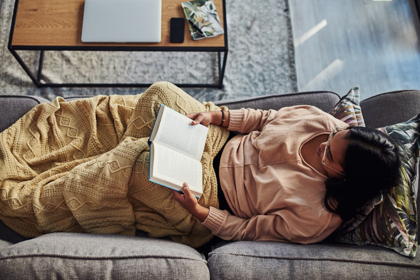High angle shot of a young woman reading a book on the sofa at home, in a story about feel good books.