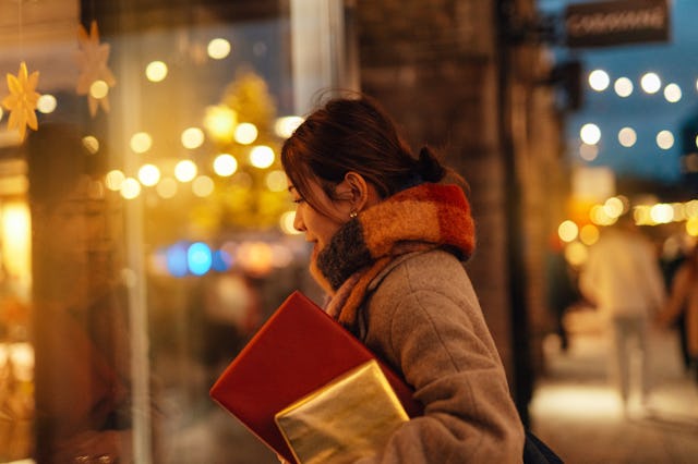 Young Asian woman carrying Christmas presents, looking at shop window during Christmas shopping at d...