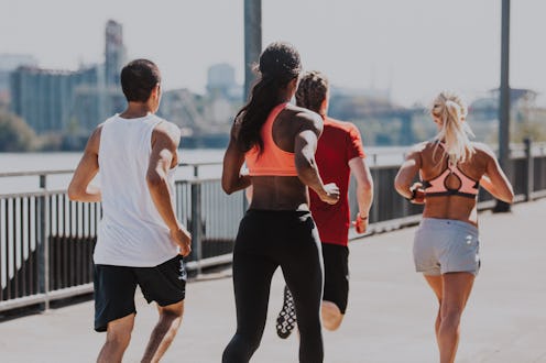 A biracial group of young adult athletes participating in a group workout, jogging down a city pathw...