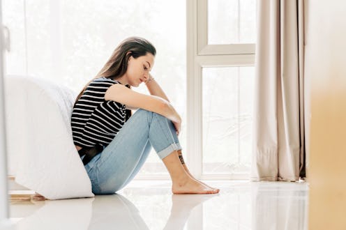 Young woman feeling sad, sitting alone on the floor of her bedroom. A scene capturing solitude and e...