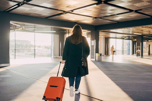 A woman with an orange suitcase walks through a sunlit airport terminal, capturing the essence of tr...