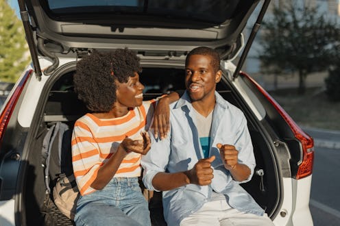 A couple relaxes in the trunk of a car, engaging in a friendly conversation. The scene conveys comfo...