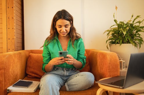 Woman sitting at home and using mobile phone. She is checking her banc account before another online...