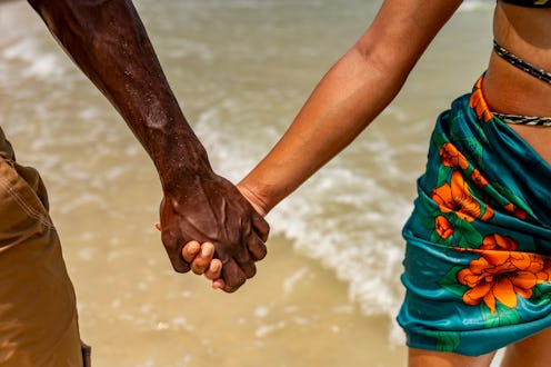Close-up of a couple holding hands while strolling on a tropical beach, symbolizing love and connect...