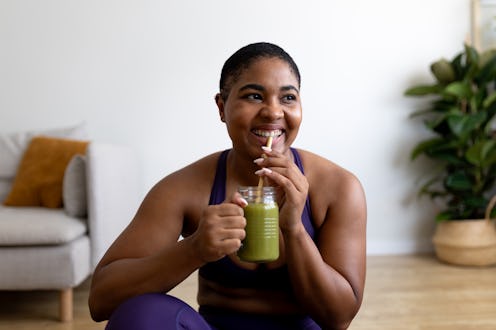 Happy young woman drinking a healthy green smoothie after exercising at home