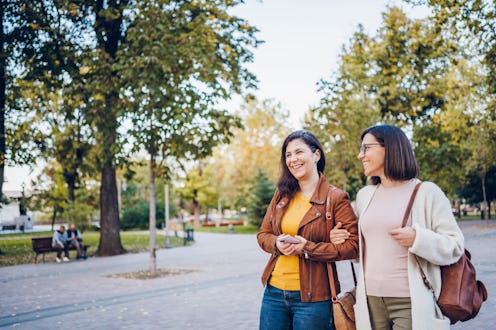 Two cheerful young woman walking through city.
They enjoying in the park in autumn. Woman friendsh...